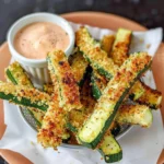 Golden crispy Air Fryer Zucchini Fries with Parmesan coating, served in a basket with creamy dipping sauce, vibrant green and golden brown colors.