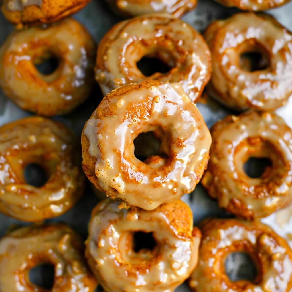 Golden-brown baked pumpkin donuts with glossy maple glaze, arranged in a cozy close-up, highlighting their tender texture and inviting autumnal appearance.