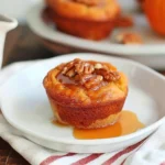 Golden-brown Baked Pumpkin French Toast Muffin topped with glossy maple syrup and crunchy pecans on a white plate, showcasing a moist, fluffy texture and inviting autumn colors.
