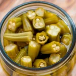 Vibrant bright-green easy pickled okra spears packed tightly in a clear glass jar, glistening in tangy brine, highlighting their crisp texture and fresh appearance.