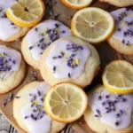 Soft golden Lemon Lavender Cookies with pale purple glaze, sprinkled with dried lavender and lemon zest, beautifully arranged beside fresh lemon slices on a rustic wooden board