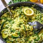 Bright, colorful Lemon Orzo With Zucchini featuring vibrant green peas, sliced zucchini, creamy orzo, and fresh lemon garnished in a non-stick skillet.