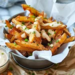 Crispy golden Louisiana Voodoo Fries topped with creamy ranch sauce, bacon, and green onions in a metal bowl, served on parchment for a vibrant, appetizing presentation.
