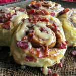 Maple Bacon Cinnamon Rolls with golden swirls, crisp bacon pieces, and maple glaze dripping on a rustic brown platter