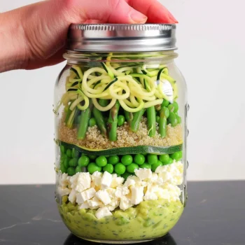 Bright, colorful layers of zucchini noodles, quinoa, asparagus, green peas, feta, and creamy dressing in a mason jar for Mason Jar Zucchini Noodle Salad with Coconut-Lime-Avocado Dressing.