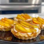 Mini Peach and Cream Cheese Tarts with golden flaky crust, fresh peach slices, and glossy honey drizzle on a dark plate, vibrant and inviting dessert presentation