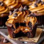 Rich chocolate Pumpkin Chocolate Peanut Butter Cupcake with glossy peanut butter frosting, chocolate chips, and a soft, gooey center on brown parchment paper.