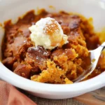 Golden-brown Pumpkin Cobbler with gooey syrup and creamy vanilla ice cream, dusted with powdered sugar in a white bowl, radiating warm, inviting fall colors and luscious textures.