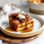 Golden Pumpkin French Toast Casserole topped with whipped cream, toasted pecans, and maple syrup, served on a white plate with rich, moist texture and autumnal hues.