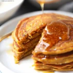 Golden pumpkin pancakes stacked on a white plate, drizzled with maple syrup, boasting fluffy layers and crispy edges for a fresh, stunning breakfast presentation.
