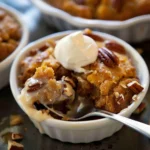 Warm Pumpkin Pecan Cobbler in white ramekin, topped with whipped cream and golden pecans, with gooey caramel sauce and a crumbly golden texture.