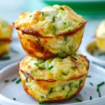Golden Savory Parmesan Zucchini Muffins with crisp, cheesy edges and flecks of green zucchini, stacked on a white plate, garnished with fresh chives.
