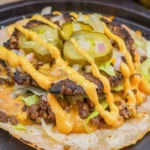 Golden brown Smash Burger Tacos topped with melty American cheese, vibrant fresh lettuce, tangy pickles, diced onions, and creamy orange Big Mac sauce drizzled artfully on a soft flour tortilla.