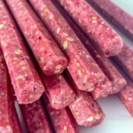 Vivid pink, creamy strawberry oat smoothie sticks for dogs with visible oat flakes, arranged in a neat stack showing their cool, smooth texture and cheerful color