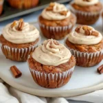 Moist Tasty Pumpkin Zucchini Muffins with creamy cinnamon cream cheese frosting, topped with cinnamon and nuts on a white plate, golden brown and beautifully swirled