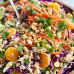 Colorful Thai Chicken Salad featuring shredded chicken, crisp green and red cabbage, carrots, mandarin oranges, cilantro, peanuts, and slivered almonds on a platter