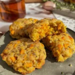 Golden maple sweet potato and sage high-protein breakfast biscuits stacked on a gray plate, showcasing vibrant orange sweet potato pieces and rustic herbs, perfect for a hearty, satisfying breakfast.