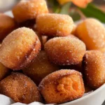 Golden mini cinnamon muffins coated with sparkling cinnamon sugar, arranged in a white bowl with a soft, pillowy texture and warm, inviting appearance.