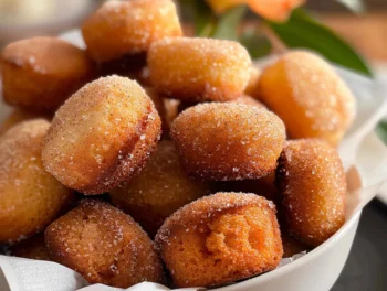 Golden mini cinnamon muffins coated with sparkling cinnamon sugar, arranged in a white bowl with a soft, pillowy texture and warm, inviting appearance.