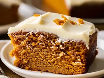 Golden orange 3-Ingredient Pumpkin Spice Cake slice with creamy white frosting on top, served on a white plate, showing moist crumb and festive presentation.