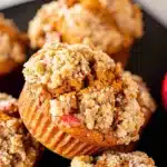 Golden-brown Apple Pumpkin Streusel Muffins with crunchy crumbly tops and fresh red apple pieces, beautifully arranged on a dark plate.