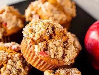 Golden-brown Apple Pumpkin Streusel Muffins with crunchy crumbly tops and fresh red apple pieces, beautifully arranged on a dark plate.