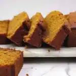 Beautifully sliced Pumpkin Bread - Rich and Buttery with golden brown crust and vibrant orange crumb, displayed on a marble board showing its moist, tender texture.