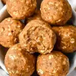 Golden pumpkin protein balls with visible oats, arranged in a white bowl, featuring soft chewy texture and rich orange hue for an inviting, wholesome snack