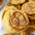 Soft golden Pumpkin Snickerdoodles with a sparkly cinnamon-sugar coating stacked on a white plate, showing crackled tops and plush texture, inviting and beautifully presented.