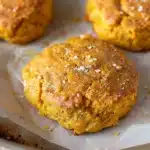 Golden, flaky Small Batch Pumpkin Biscuits with a warm orange hue and sprinkled sea salt, arranged beautifully on parchment-lined baking sheet.