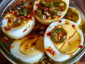 A close-up of halved Hot and Spicy Garlic Pickled Eggs with jalapeño slices, red pepper flakes, and vibrant brine in a glass jar, showcasing their colorful and appetizing appearance.
