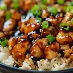 Close-up of Honey BBQ Chicken Rice with glossy sauce, vibrant green onions, and fluffy rice in a dark bowl.