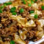 Hearty low-carb Mongolian ground beef and cabbage dish garnished with green onions and sesame seeds, presented on a white plate.