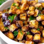 Crispy, golden-brown air fryer eggplant cubes garnished with fresh herbs in a white bowl