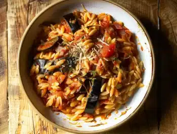 Close-up photo of one pot eggplant parmesan orzo with tomato sauce, Parmesan, and herbs in a rustic bowl on wooden table