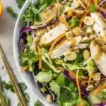 Close-up of Easy Healthy Asian Chicken Salad with ginger dressing featuring chicken, greens, nuts, and mandarin oranges.