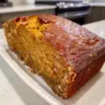 Close-up of moist, golden brown homemade DIY pumpkin bread loaf on white serving plate in modern kitchen