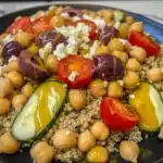 Close-up of colorful Mediterranean quinoa bean salad with chickpeas, tomatoes, cucumbers, olives, and feta on a black plate