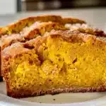 Close-up of moist pumpkin bread slices with warm spices on a white plate, showcasing soft texture and golden crust