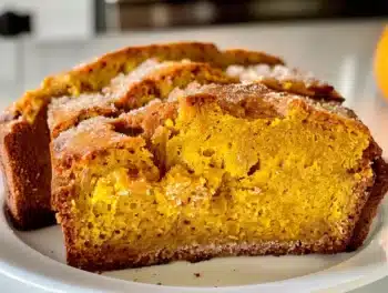 Close-up of moist pumpkin bread slices with warm spices on a white plate, showcasing soft texture and golden crust