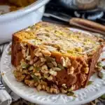 Close-up of a slice of homemade pumpkin bread topped with chopped walnuts and pumpkin seeds on a white plate