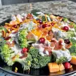 Broccoli Salad with creamy dressing, cheddar cheese cubes, bacon, sunflower seeds, and cranberries on a black plate.