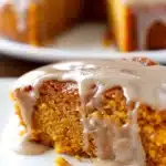 Close-up of moist pumpkin cake slice drizzled with shiny apple cider glaze, showcasing soft texture and rich autumn colors on a white plate.