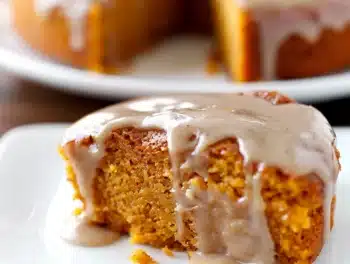 Close-up of moist pumpkin cake slice drizzled with shiny apple cider glaze, showcasing soft texture and rich autumn colors on a white plate.