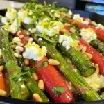 Rainbow carrots and asparagus roasted with fresh herbs, pine nuts, and crumbled goat cheese on a black platter.