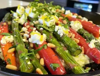 Rainbow carrots and asparagus roasted with fresh herbs, pine nuts, and crumbled goat cheese on a black platter.