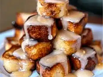 Golden-brown cinnamon roll French toast bites stacked and drizzled with sweet icing, tempting and inviting for a dreamy breakfast.