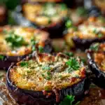 Close-up of crispy baked eggplant slices topped with Parmesan and parsley on a baking tray