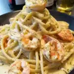 A blissful serving of linguine tossed in creamy shrimp sauce and topped with fresh parsley and lemon zest on a black plate.