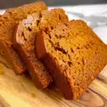 Thick slices of homemade pumpkin bread with a golden, moist crumb on a wooden board.